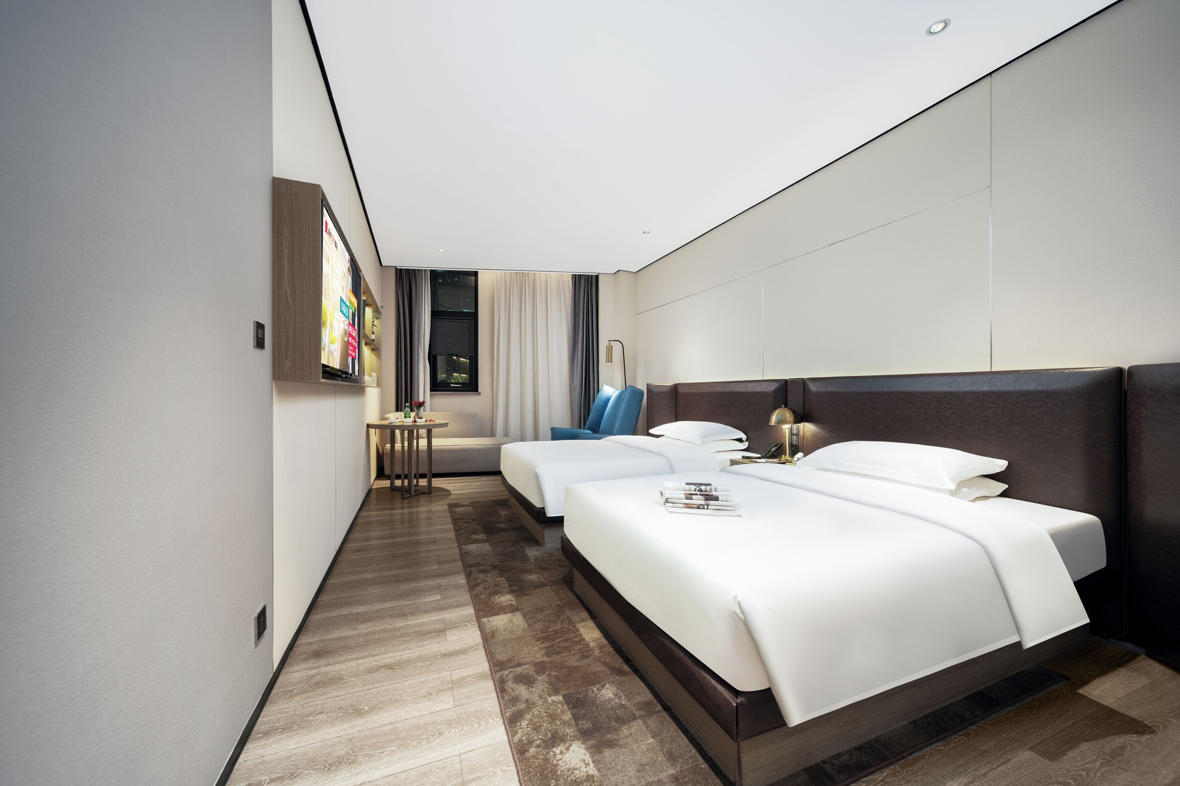 A modern hotel room with a large bed, a smaller bed, a desk, and a window with curtains.