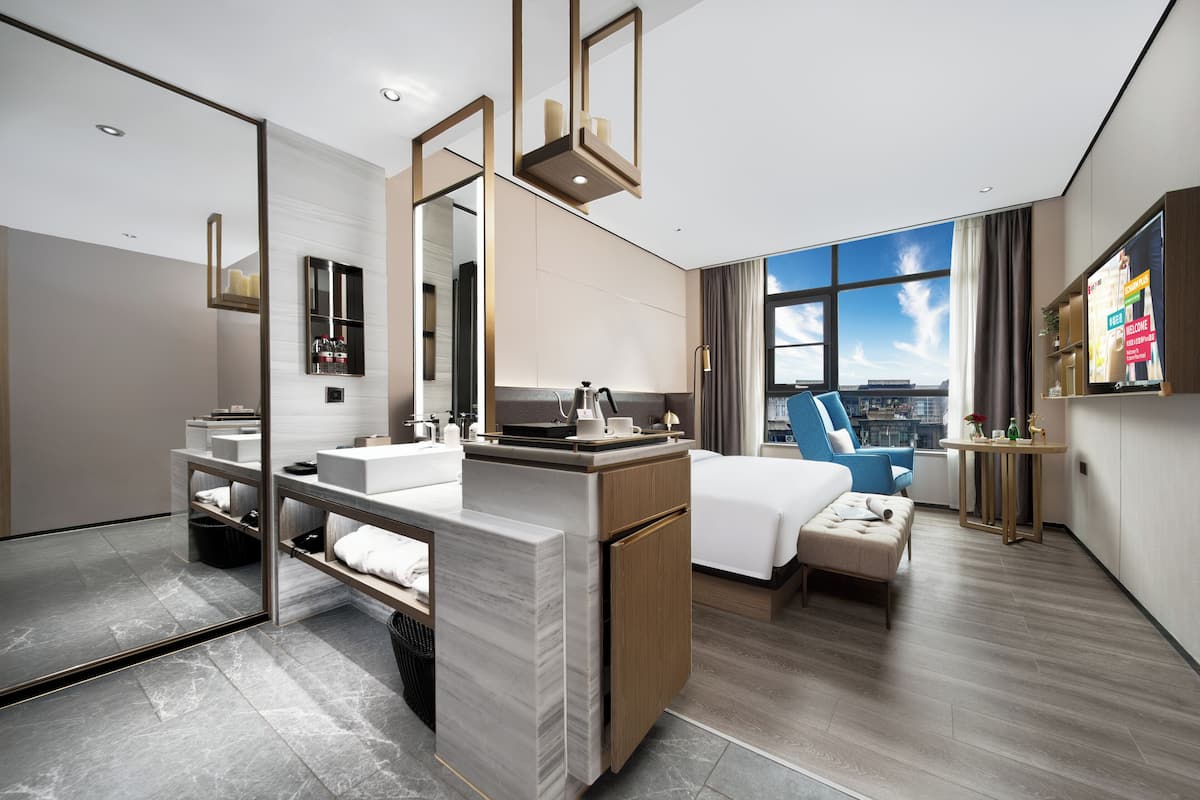 A modern hotel room with a large mirror, a bed, a small table, and a view of the city.