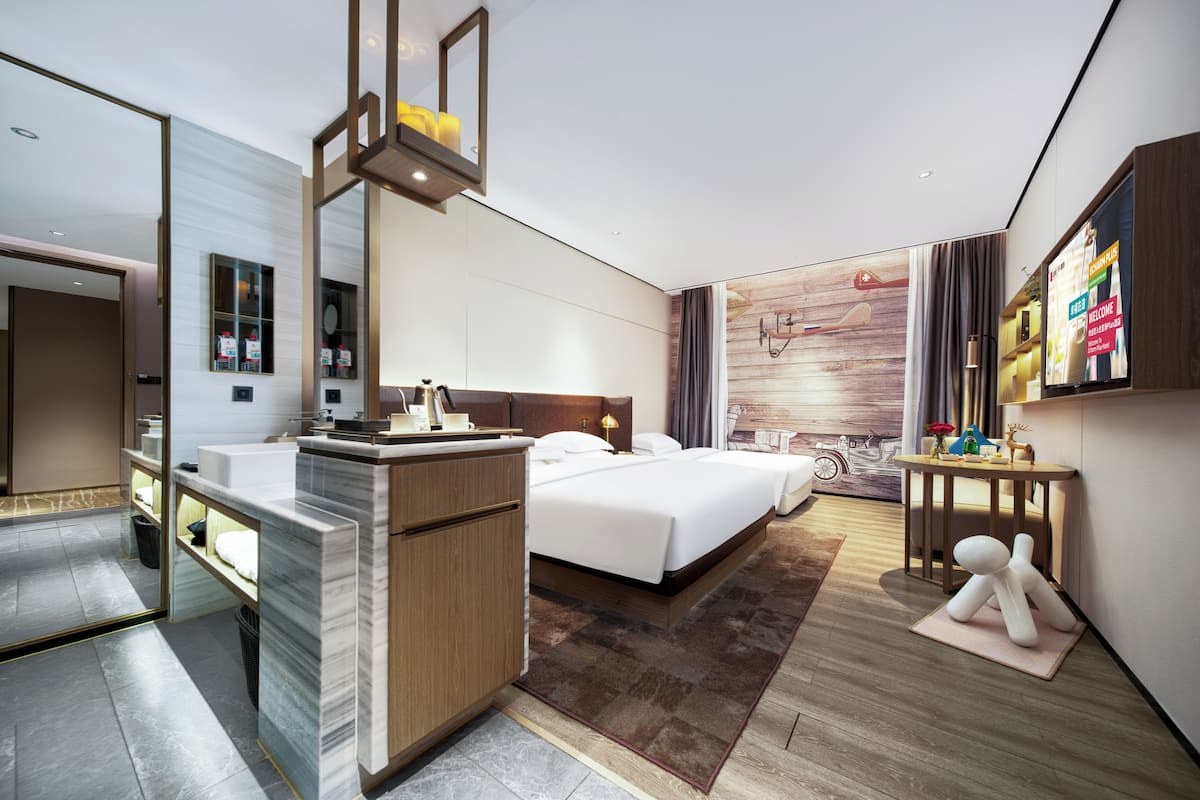 A modern hotel room with a bed, a desk, a mirror, and a wall-mounted TV.