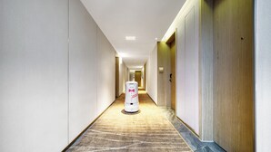Un couloir d’hôtel avec un sol recouvert de moquette, une poubelle et une porte sur la droite.