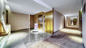 Un couloir d’hôtel moderne avec un aspirateur robot, des ascenseurs et un sol ciré.