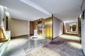 En modern hotellkorridor med en robotdammsugare, hissar och ett polerat golv.