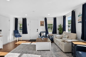 A living room with a white sofa, a blue armchair, a coffee table, and a window with curtains. - New Vermilion 1st Floor Getaway-walk to downtown & waterfront! (Vermilion)