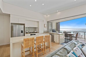 A modern kitchen with a large island, a dining area with a view, and a balcony overlooking the ocean. - Waves 15 - Beachfront with pool (Point Lookout)