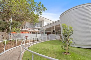 Ein Hotel mit modernem Design, das einen überdachten Außenbereich mit Sonnenschirmen, einen grünen Innenhof und eine große zylindrische Struktur zeigt.