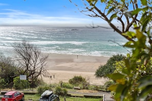A beach with a person walking, a red car, and a sign in the foreground. - Waves 15 - Beachfront with pool (Point Lookout)