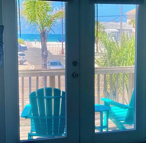 A view from a balcony with a table and chairs, a palm tree, and a beach in the background.