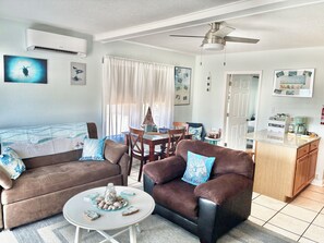 A living room with a brown sofa, a brown armchair, a small round table, a ceiling fan, and a kitchen area with a coffee maker. - Cozy 1-bedroom on Gulf Blvd Madeira Beach, 5 min walk to John’s Pass (Madeira Beach)