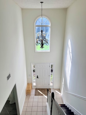 Una escalera conduce a un rellano con una puerta blanca, un candelabro y vistas a través de una ventana.