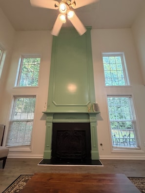Una habitación con chimenea, ventilador de techo y dos ventanas con persianas.