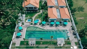 Vista aérea de un resort con piscina, sillones de descanso y palmeras.