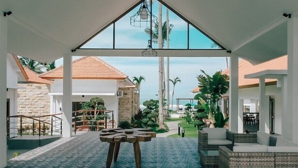 Un espacio al aire libre cubierto con vista a una casa, una mesa de madera y mobiliario de mimbre.