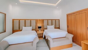 Una habitación de hotel con dos camas, un armario de madera y una mesita de noche con lámpara.