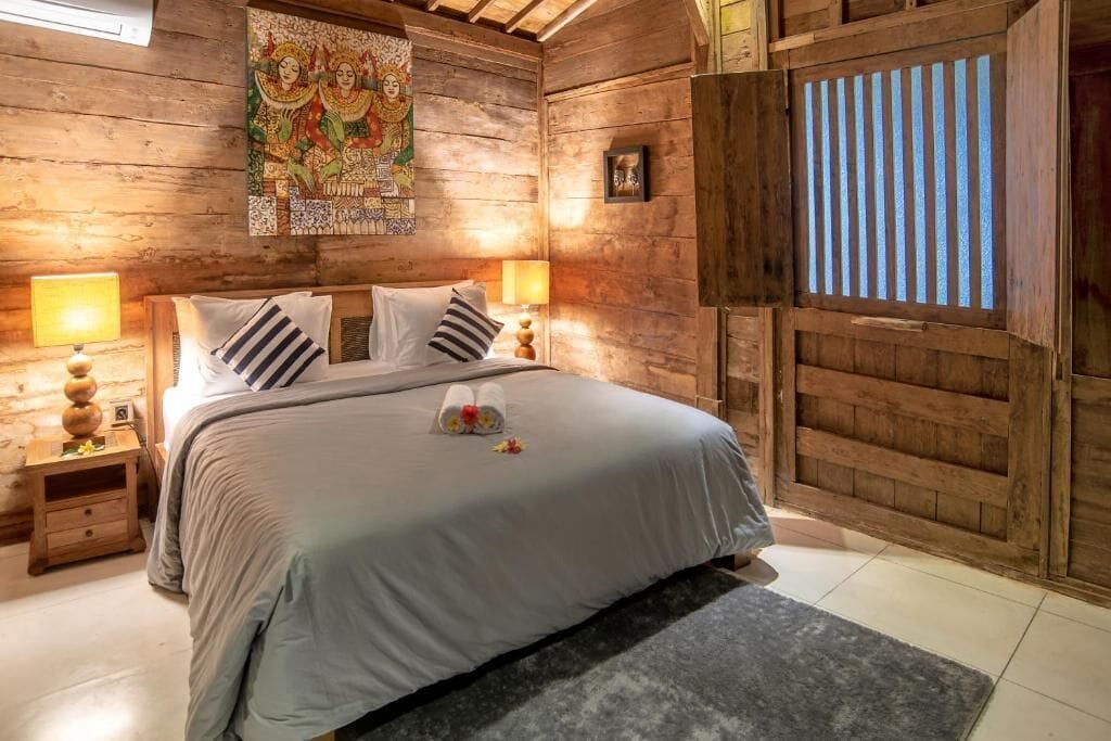 Une pièce en bois comprenant un lit, deux tables de chevet, un tableau mural et une fenêtre avec des stores verticaux.