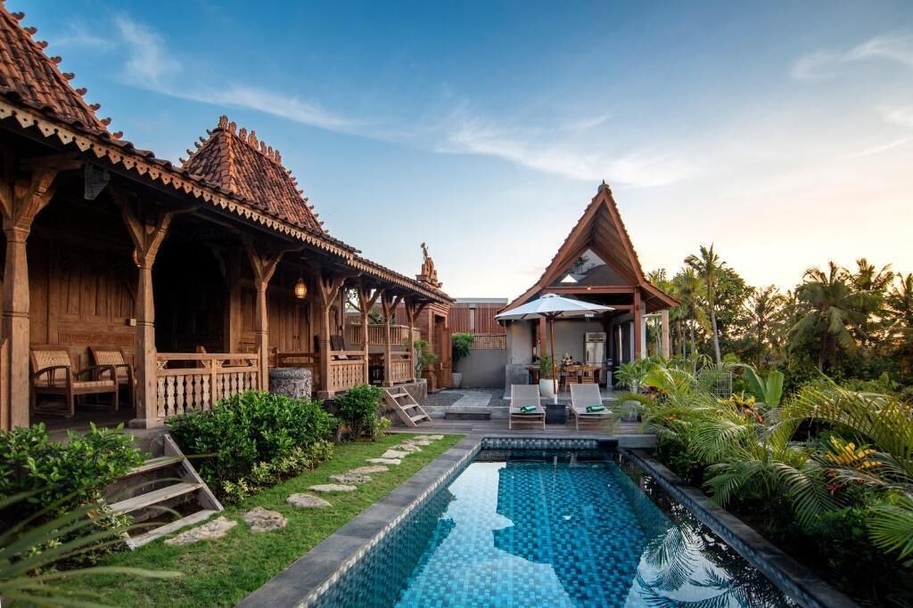 A pool with a wooden deck, a covered seating area, and a traditional building with a tiled roof.