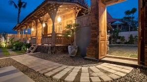 A wooden structure with a covered seating area, a stone pathway, and a view of the surrounding landscape.