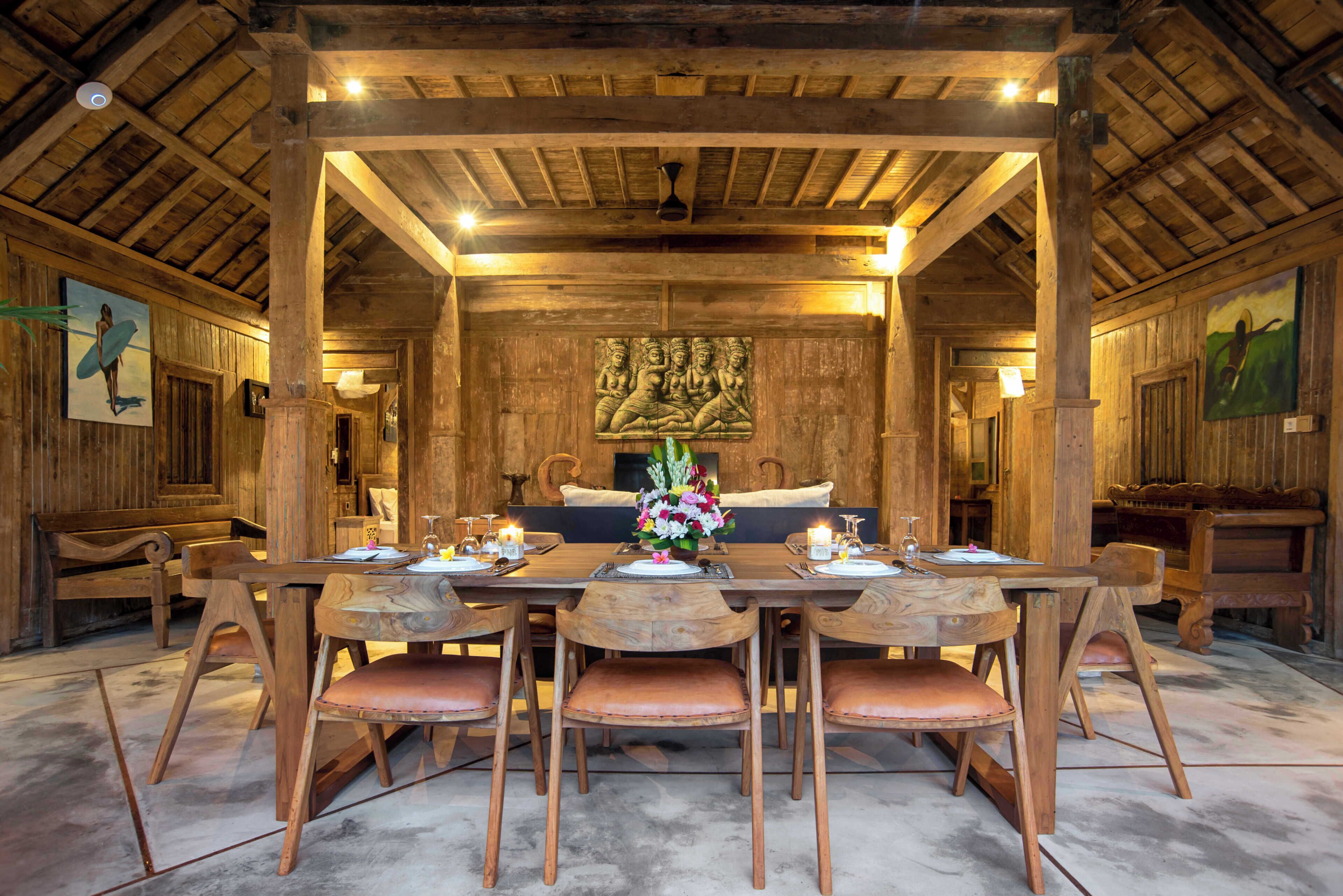 A wooden dining room with a high ceiling, a central table set for six, and a fireplace in the background.