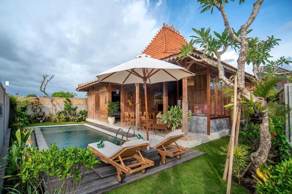 A poolside area with a covered seating area, a pool, and lush greenery.