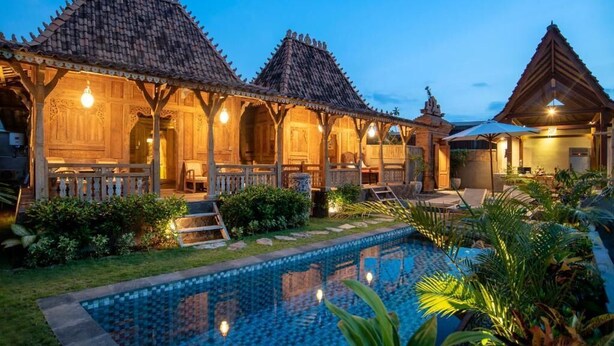 A traditional wooden building with a swimming pool, surrounded by lush greenery.