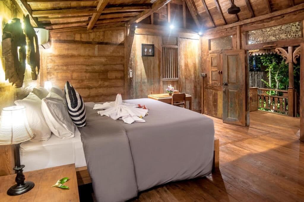 A wooden room with a bed, a table with a lamp, and a door leading to a balcony.