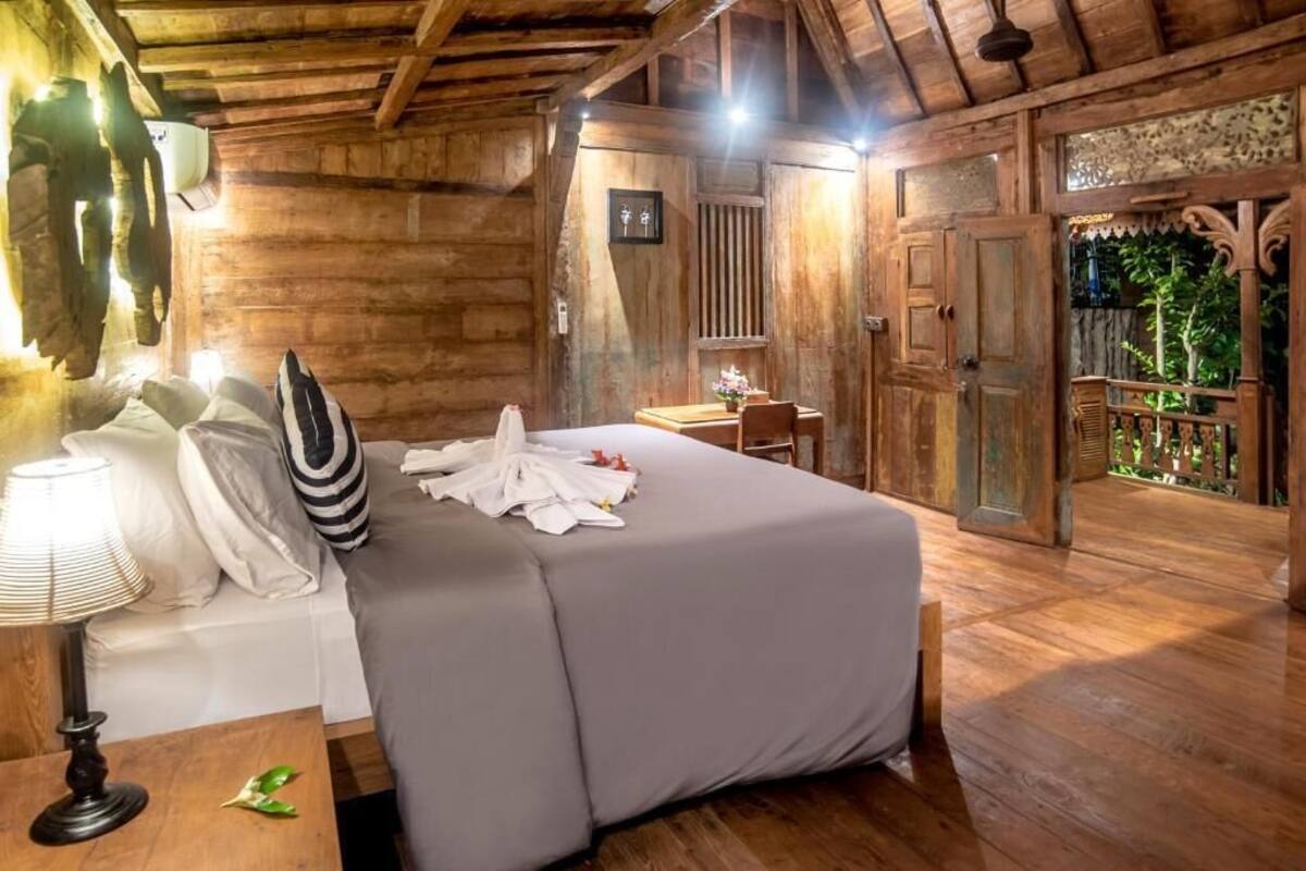 A wooden room with a bed, a table with a lamp, and a door leading to a balcony.