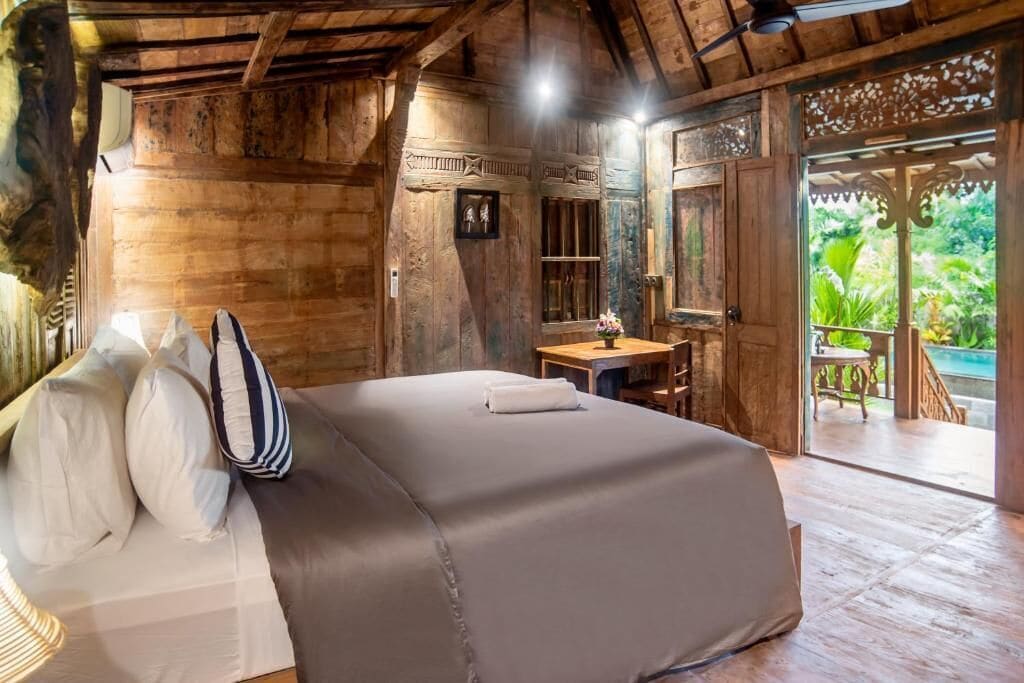 A wooden room with a bed, a desk, and a view of greenery outside.