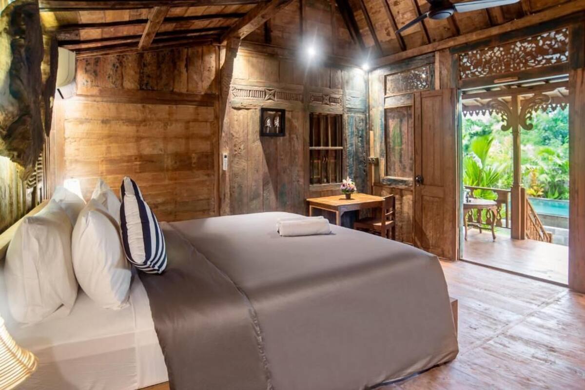 A wooden room with a bed, a desk, and a view of greenery outside.