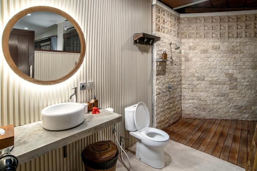 A bathroom with a round mirror, a white sink, a toilet, and a shower area.