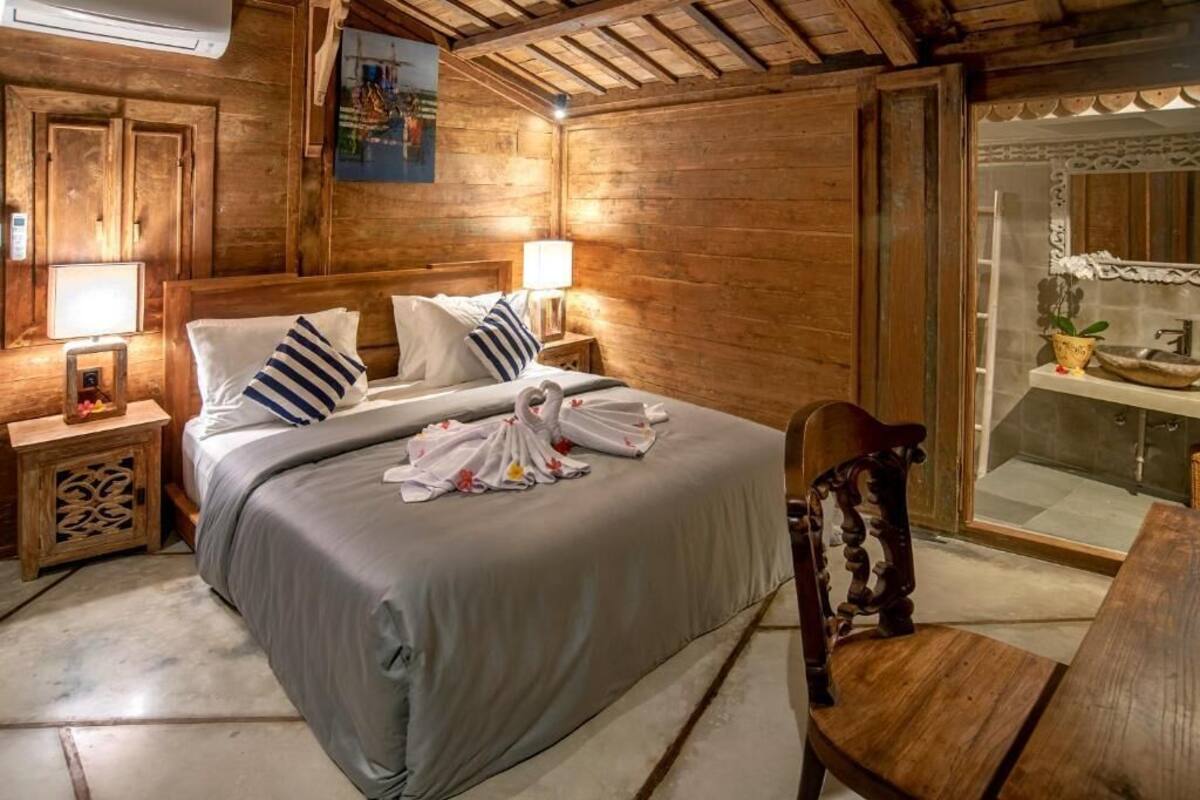 A wooden room with a bed, nightstands, a chair, and a bathroom visible through a glass door.
