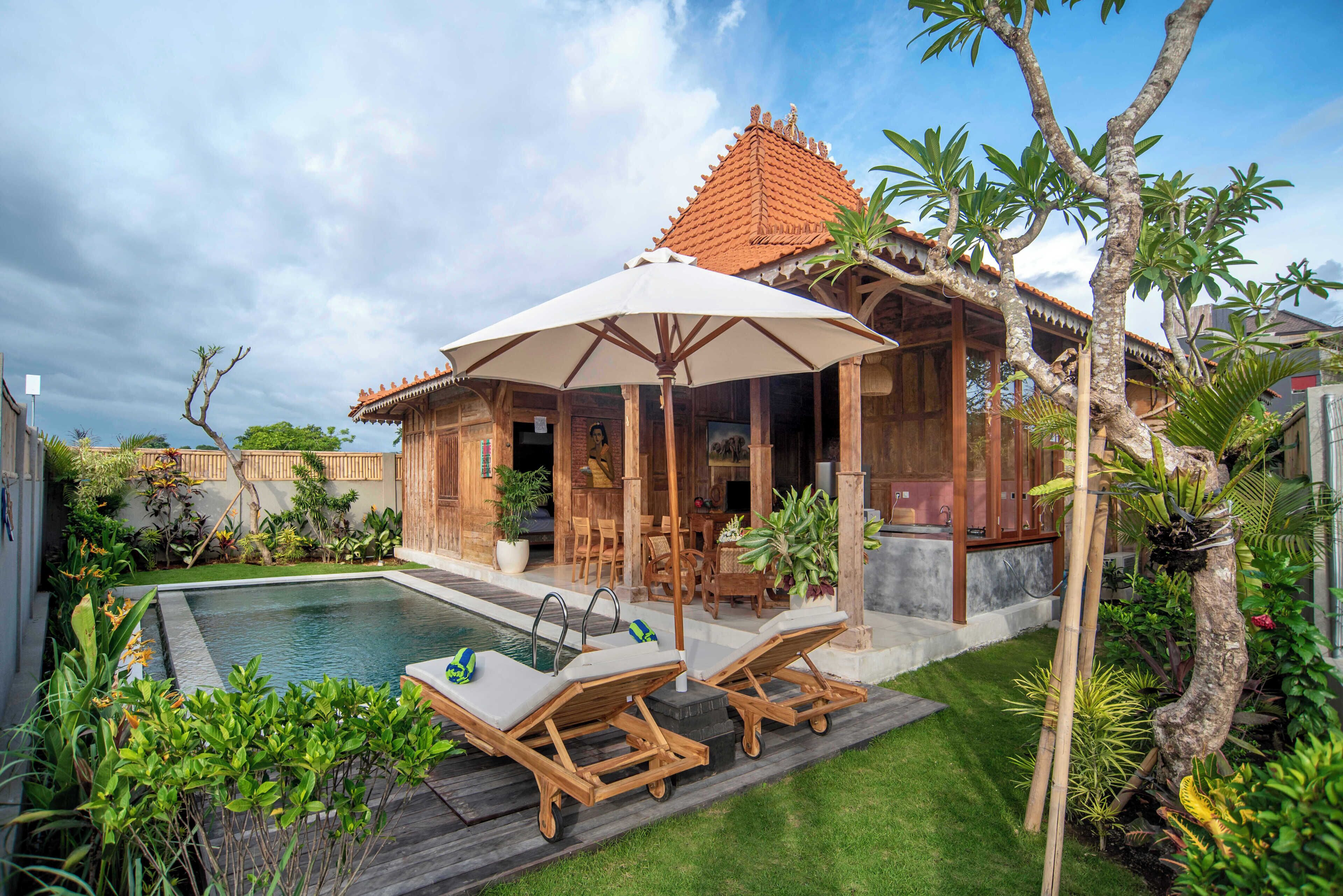 A poolside area with lounge chairs, a covered seating area, and a wooden structure with a tiled roof.
