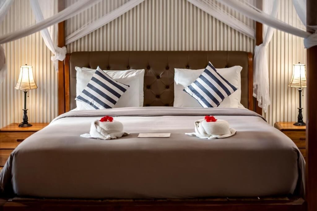 A hotel room with a large bed, striped pillows, a canopy, and two bedside lamps.