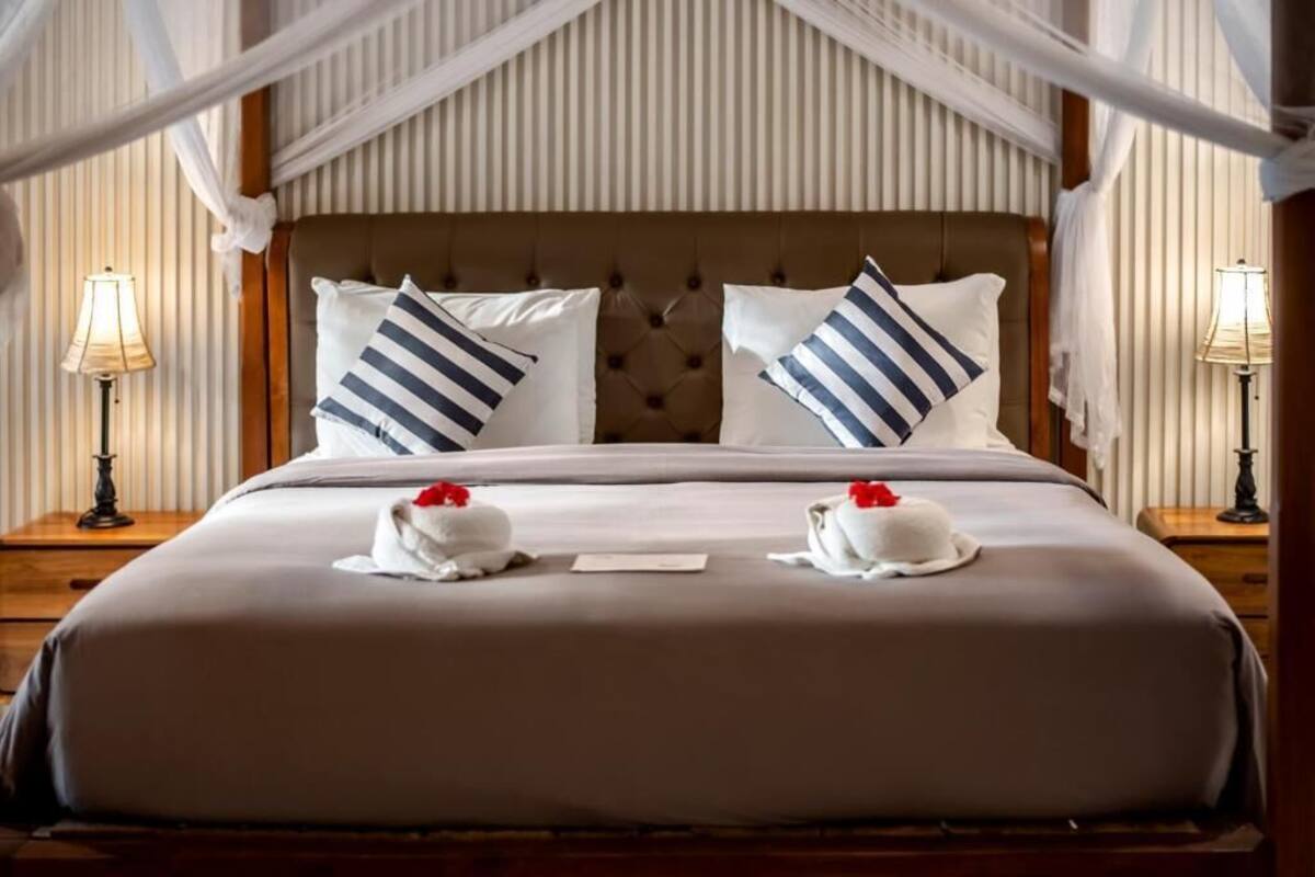 A hotel room with a large bed, striped pillows, a canopy, and two bedside lamps.