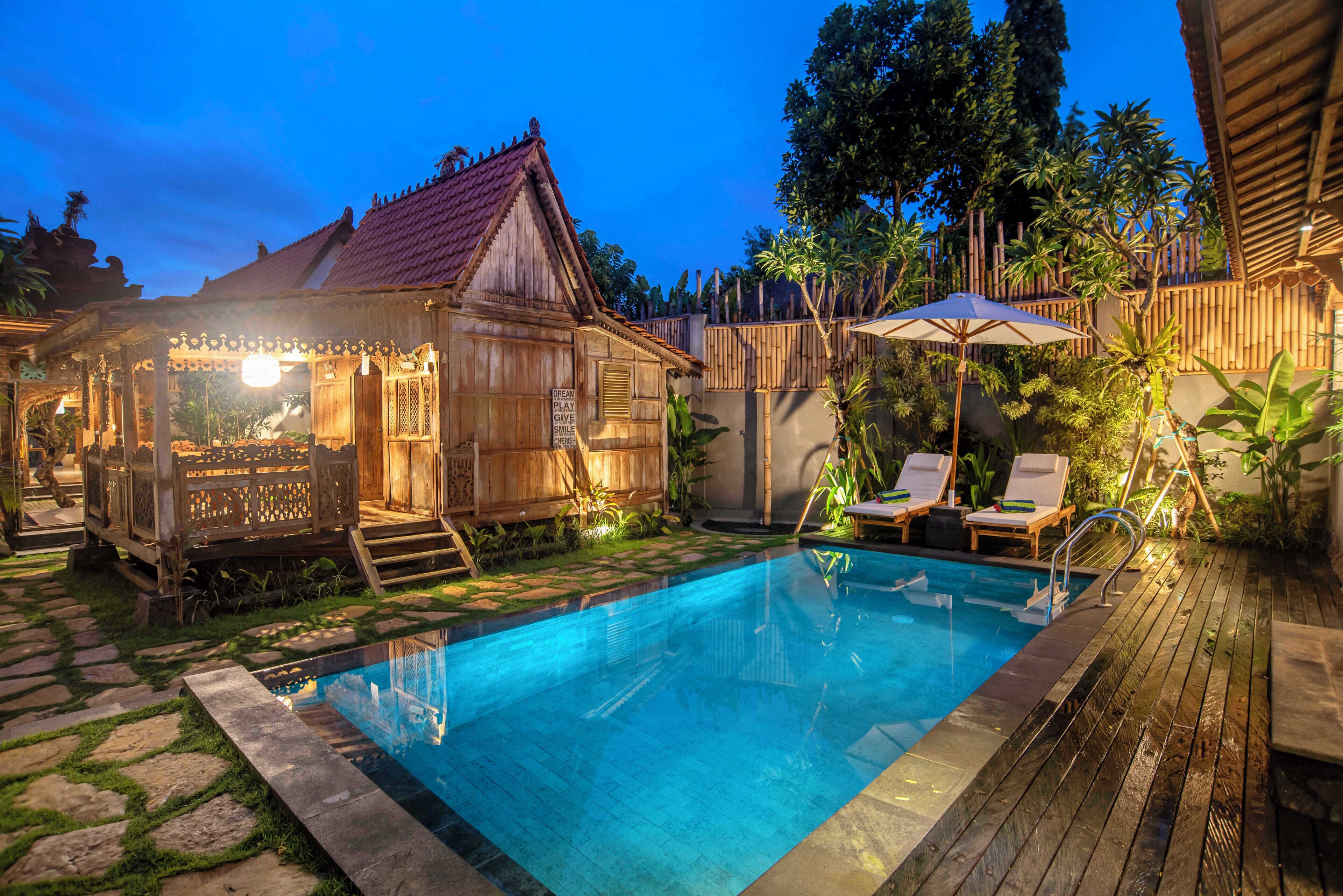 A wooden pool area with a pool, lounge chairs, and a small wooden structure with steps leading to a door.