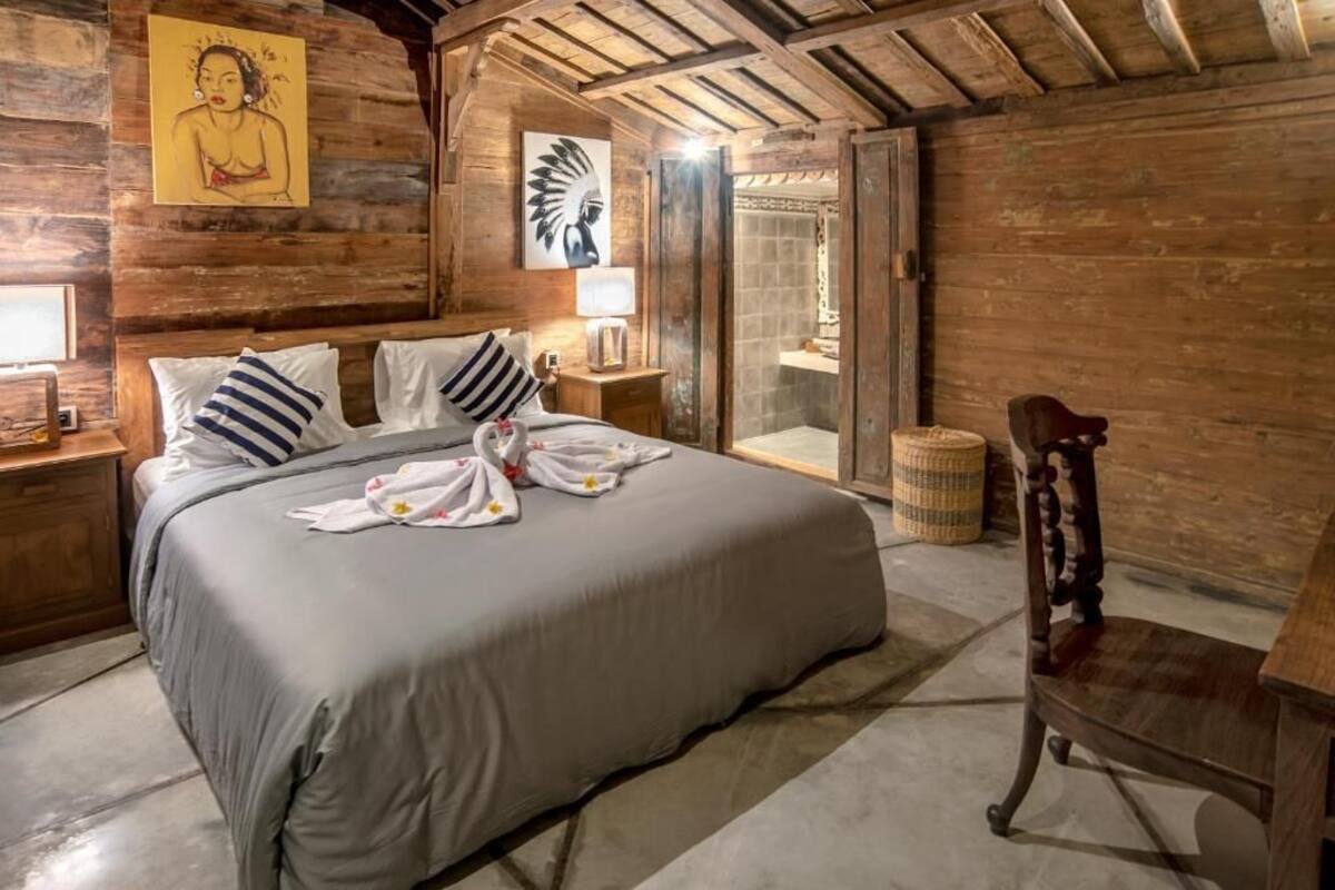A wooden room with a bed, a chair, and artwork on the walls.