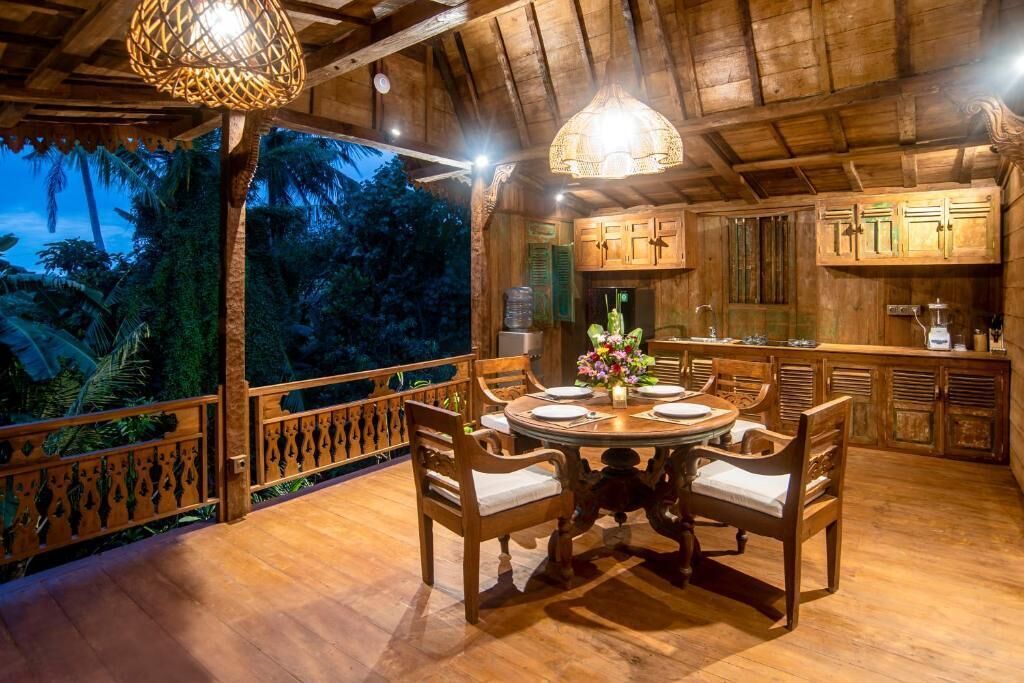 A wooden dining area with a round table and chairs, a hanging light fixture, and a view of the outdoors.