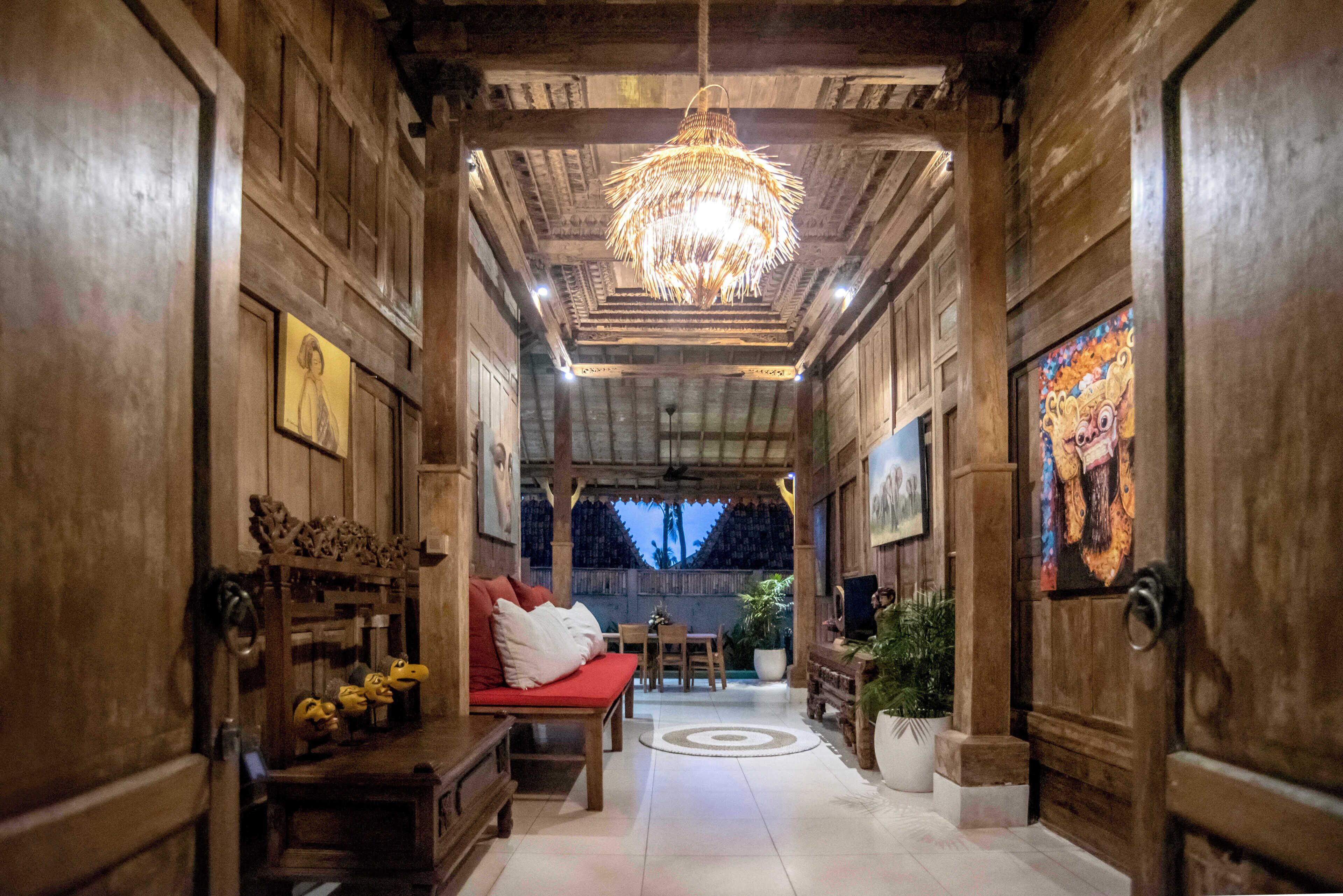A wooden interior with a chandelier, a sofa, a dining table, and a TV.