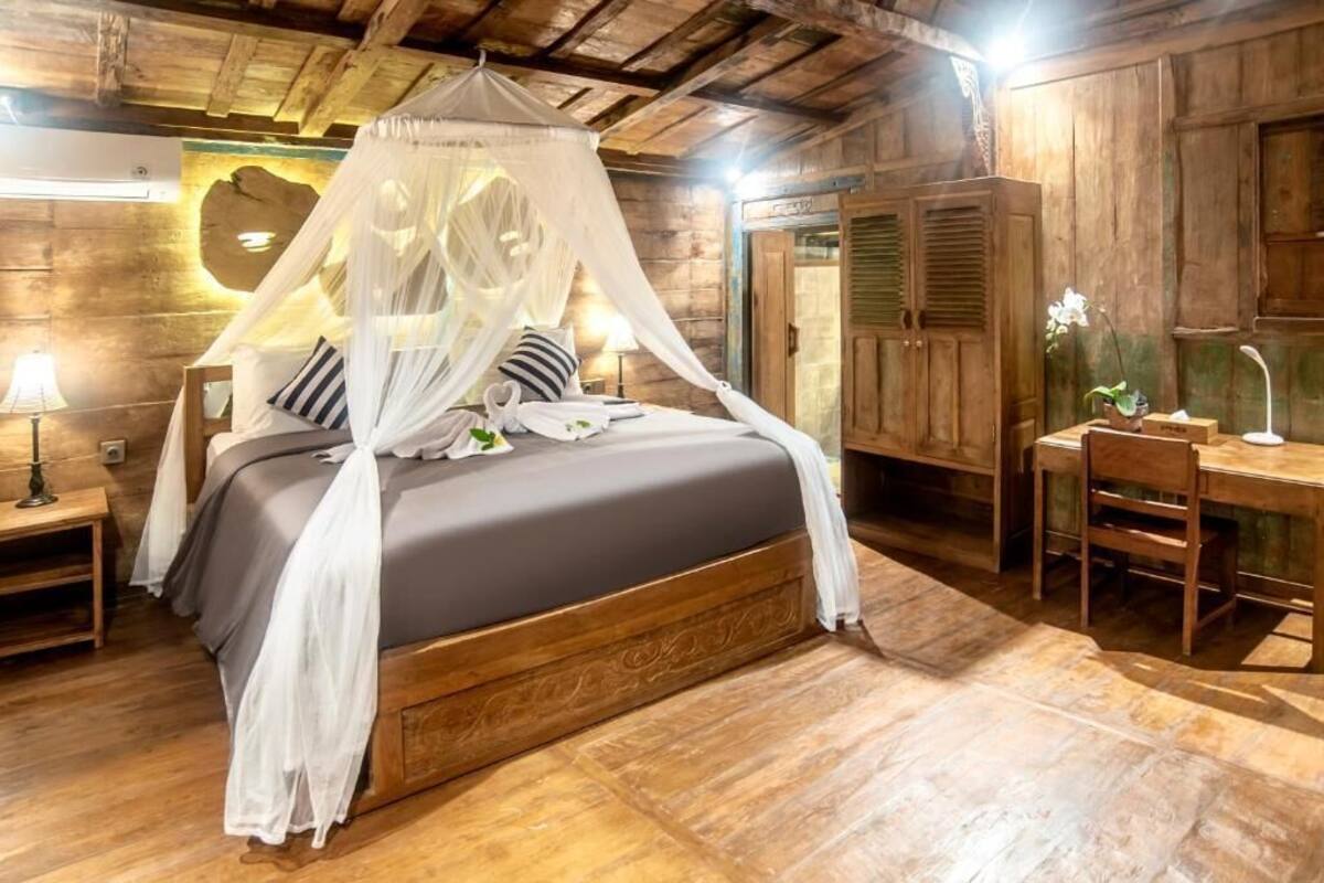 A wooden bedroom with a canopy bed, a desk, and a chair.