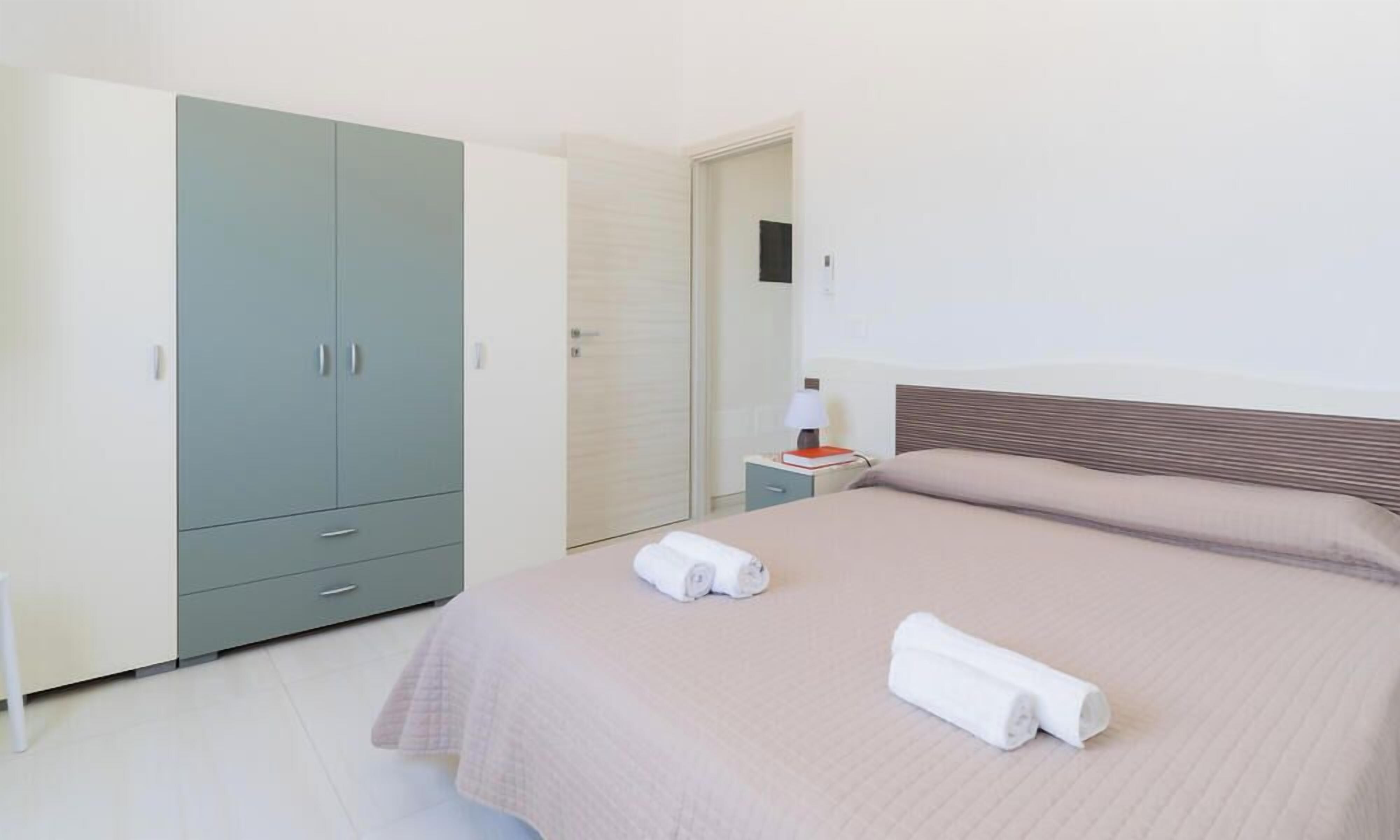 A bedroom with a bed, a wardrobe, a nightstand, and a lamp.