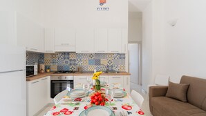 A modern kitchen with white cabinets, a tiled backsplash, and a dining table set with plates, glasses, and a centerpiece. - Villa Paradiso by Vivimy (Capilungo)