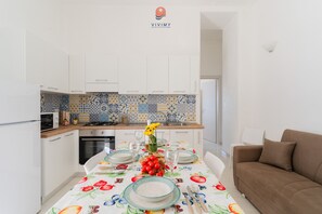 A modern kitchen with white cabinets, a tiled backsplash, and a dining table set with plates, glasses, and a centerpiece. - Villa Paradiso by Vivimy (Capilungo)