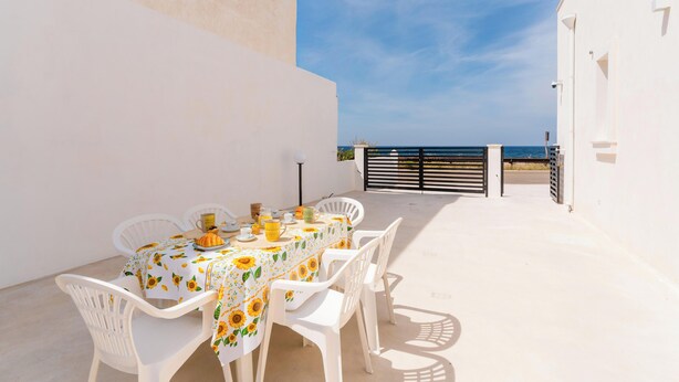 A sunlit outdoor dining area with a table set for two, white chairs, and a view of the sea. - Villa Paradiso by Vivimy (Capilungo)
