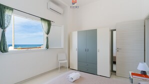 A bedroom with a bed, a chair, a wardrobe, a bedside table with a lamp, and a window with curtains. - Villa Paradiso by Vivimy (Capilungo)