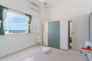A bedroom with a bed, a chair, a wardrobe, a bedside table with a lamp, and a window with curtains. - Villa Paradiso by Vivimy (Capilungo)