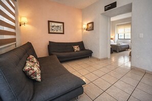 Ein Hotelzimmer mit zwei dunklen Sofas, einem gefliesten Boden und einem Bett im Hintergrund.