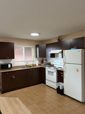 Una cocina con armarios de madera oscura, un refrigerador blanco, una estufa y un microondas.