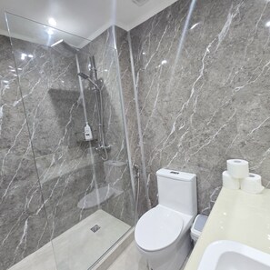 Een moderne badkamer met een glazen douche, een toilet en een wastafel met toiletpapier.