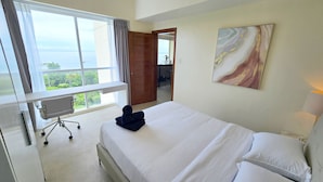 Une chambre d’hôtel avec un lit, un bureau et une chaise. Il y a une fenêtre donnant sur un espace verdoyant et un bâtiment.