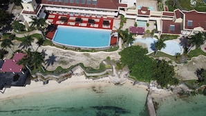 Vue aérienne d’un complexe hôtelier doté d’une grande piscine, d’une plage et de plusieurs bâtiments aux toits rouges.