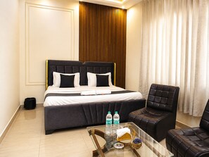 A hotel room with a bed, two chairs, a small table with bottles and glasses, and a curtain. - Hotel sudan inn kalka shimla higway (Zirakpur)