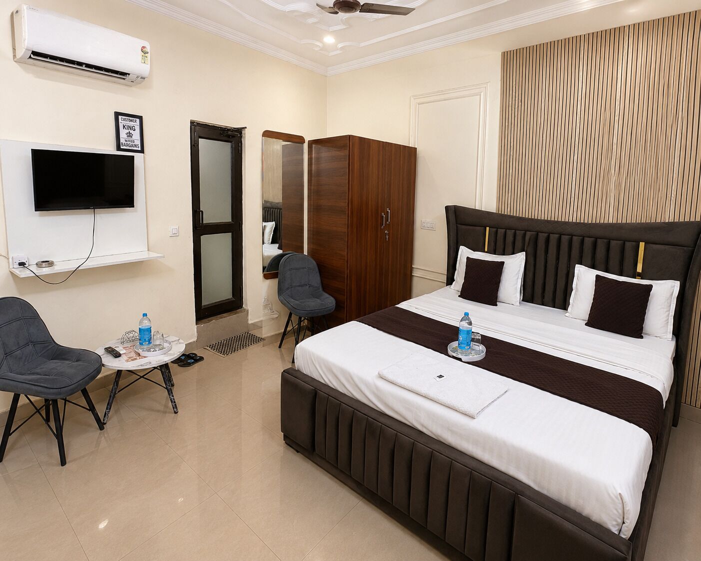 A hotel room with a bed, a desk, a chair, an air conditioning unit, a television, and a wardrobe.